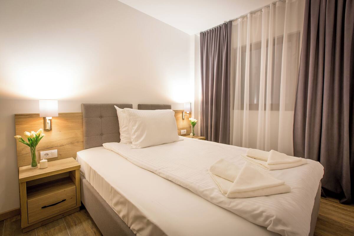 Hotellihuone, jossa on sänky, yöpöydät, lamput ja verhot.