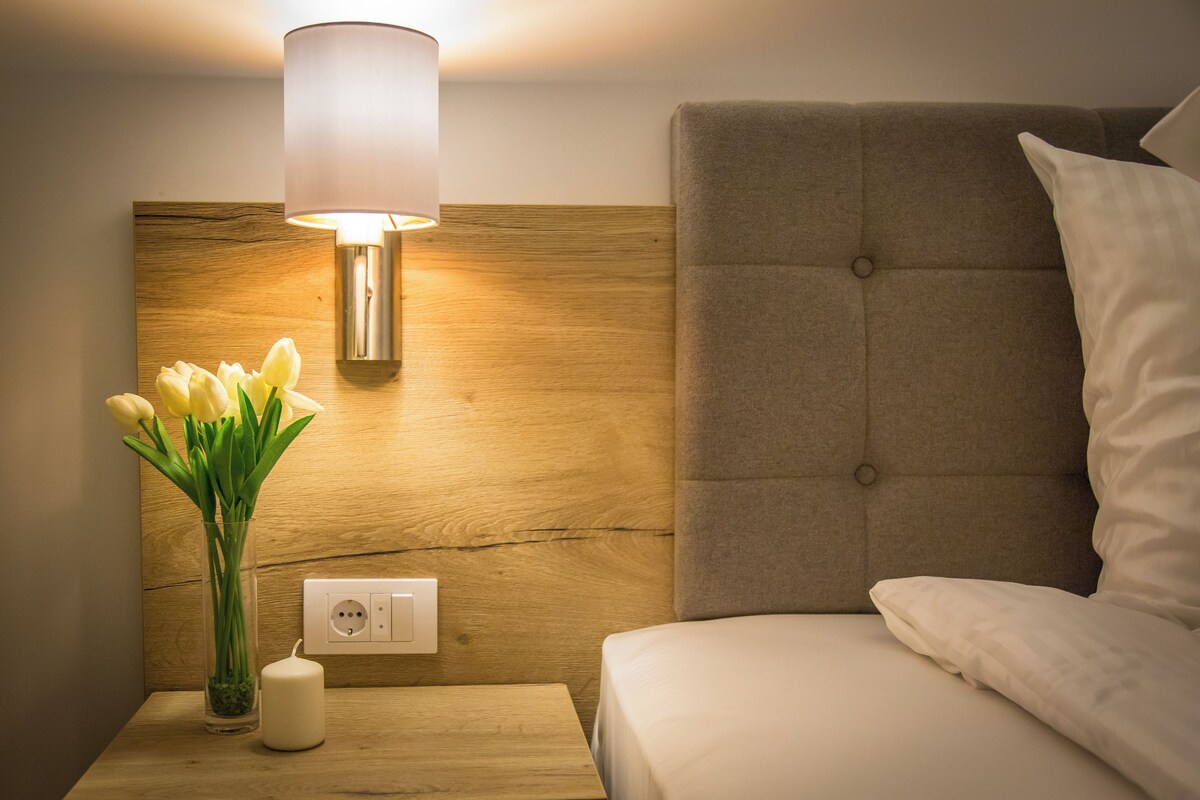 A hotel room with a wooden headboard, a bedside lamp, a vase with flowers, and a power outlet.