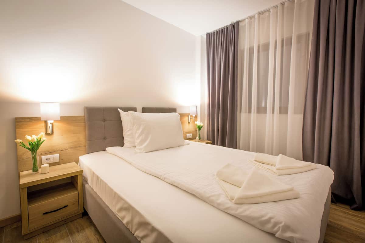 Hotellihuone, jossa on sänky, yöpöydät, lamput ja verhot.