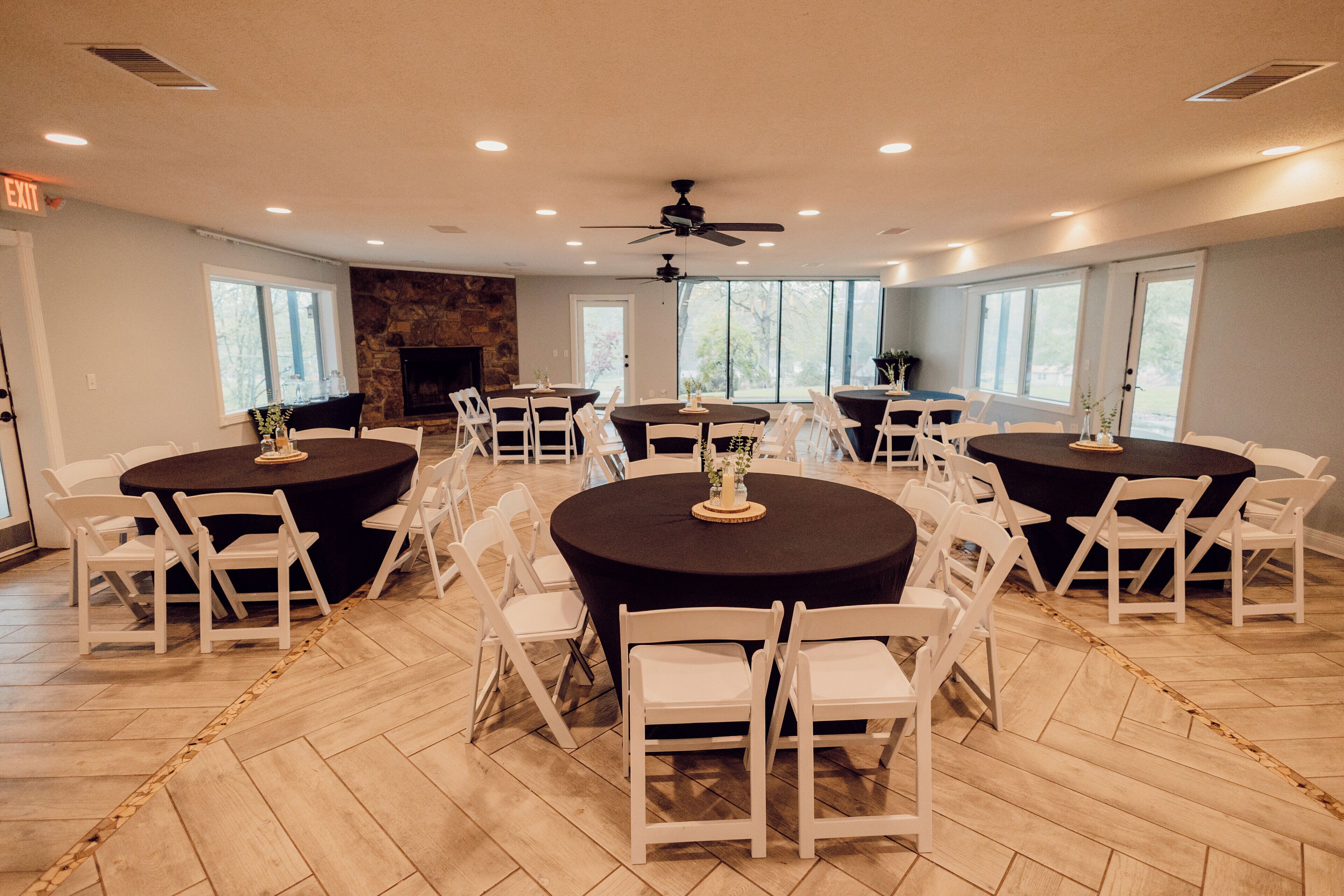 A spacious room with multiple round tables, white chairs, and a stone fireplace.