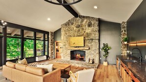 Una sala de estar moderna con chimenea de piedra, ventanas amplias, un sofá y un comedor.