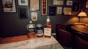 Three bottles of whiskey on a wooden table in a bar setting with framed pictures on the wall.