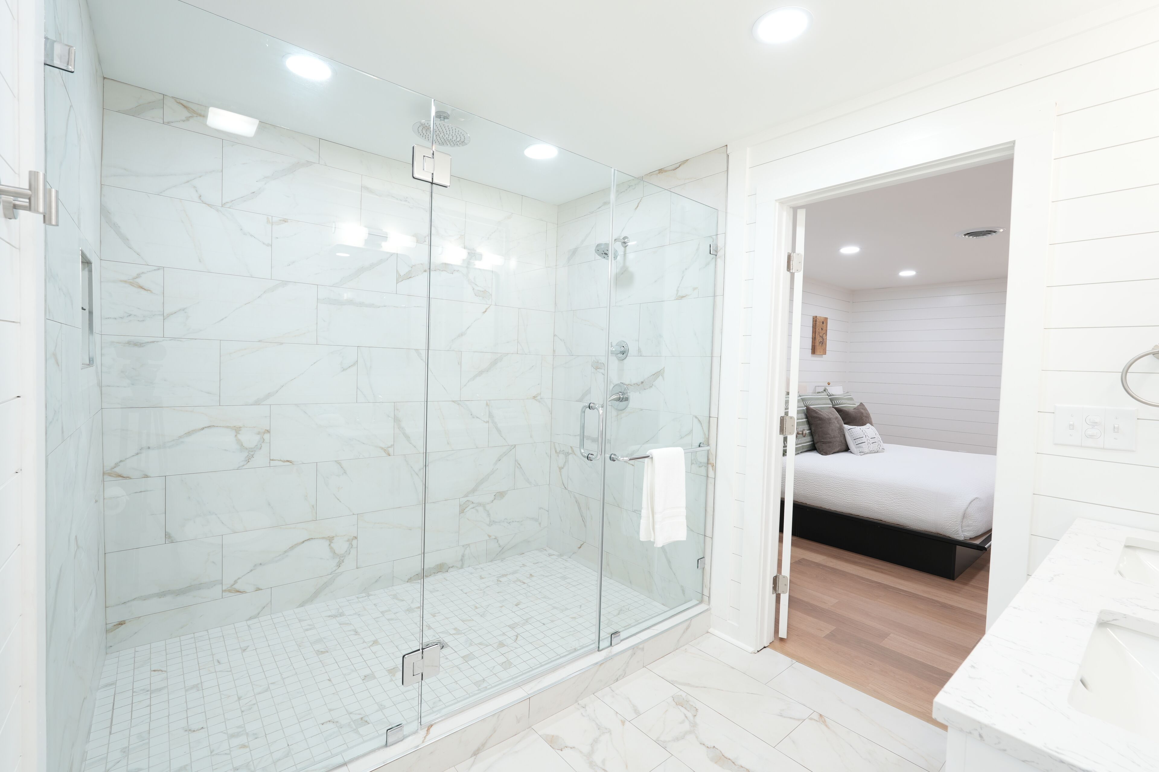 Un baño moderno con ducha envuelta en vidrio, lavamanos blanco y suelo de madera.