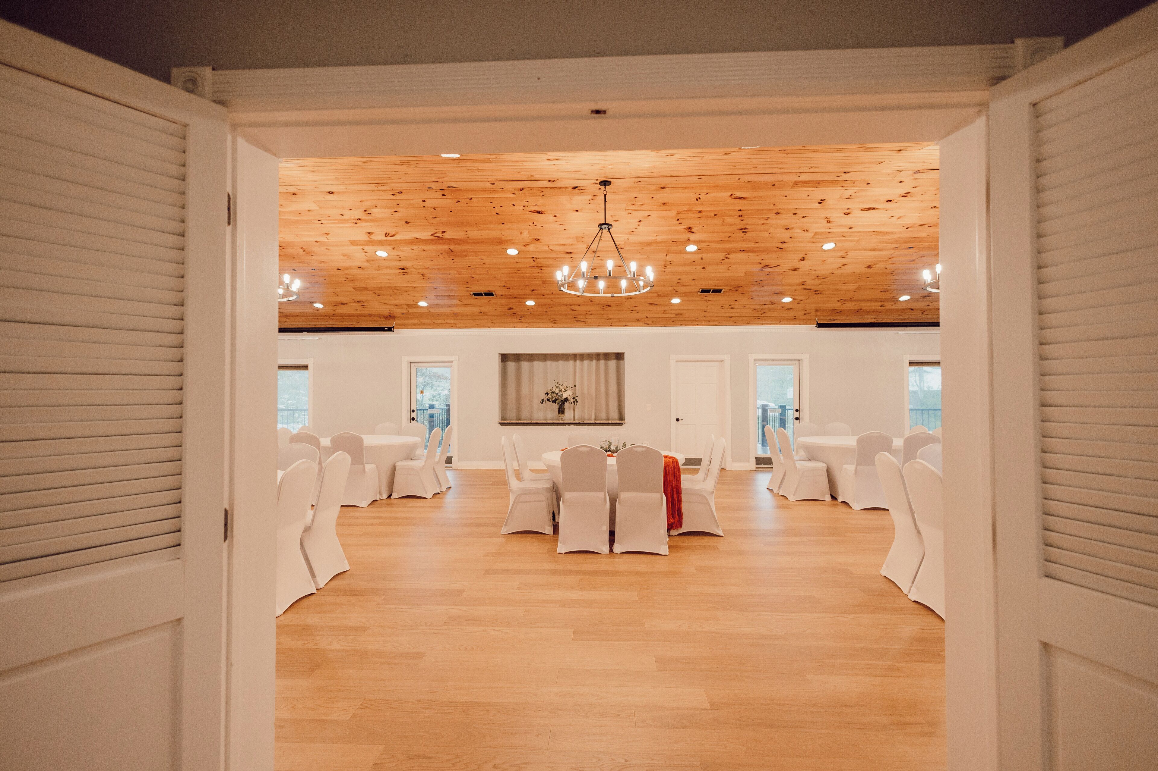 Une pièce spacieuse dotée d’un plancher en bois et d’un plafond haut, avec une table centrale entourée de chaises et un lustre.