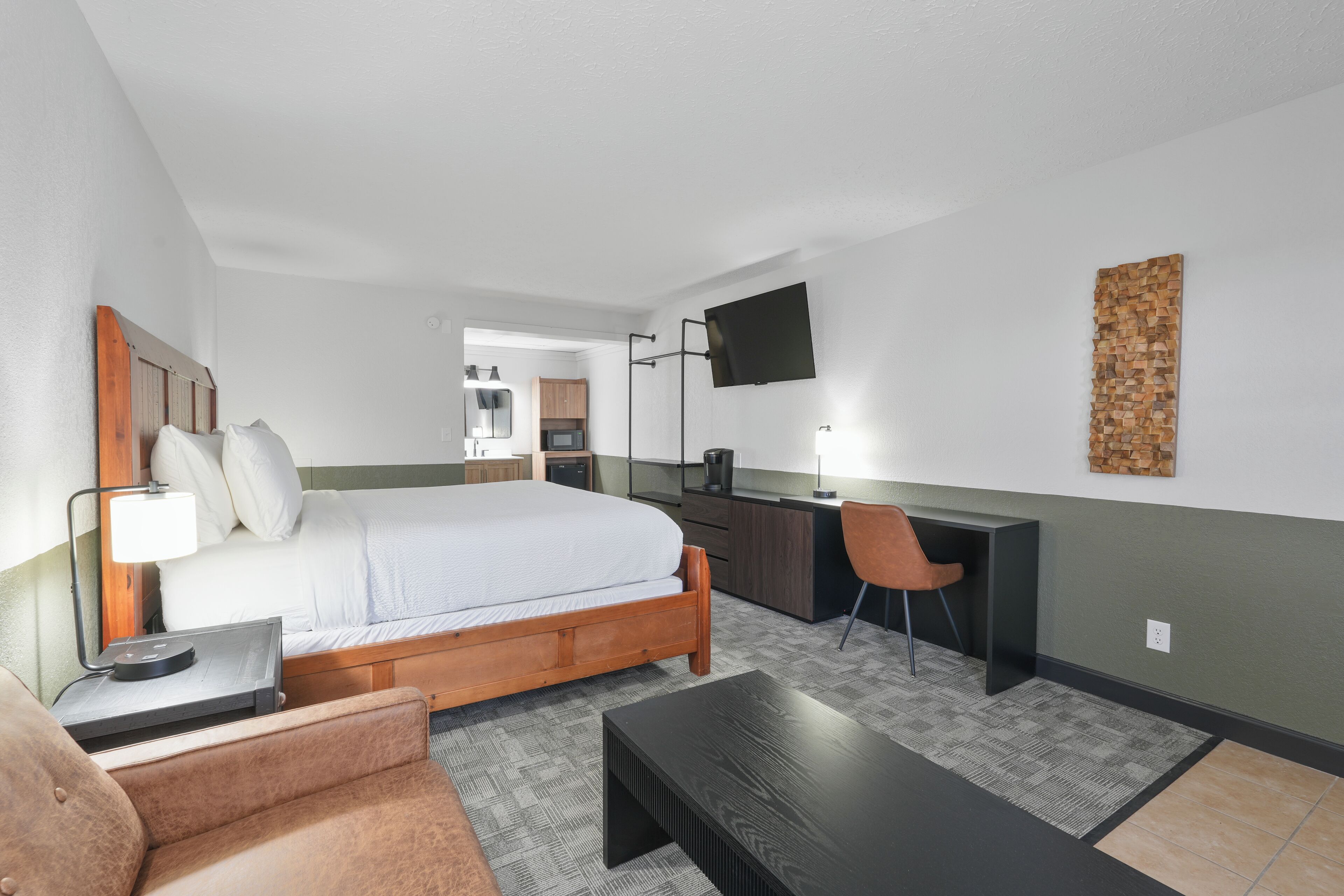 Een slaapkamer met een bed, bureau, stoel en een aan de muur bevestigde televisie.