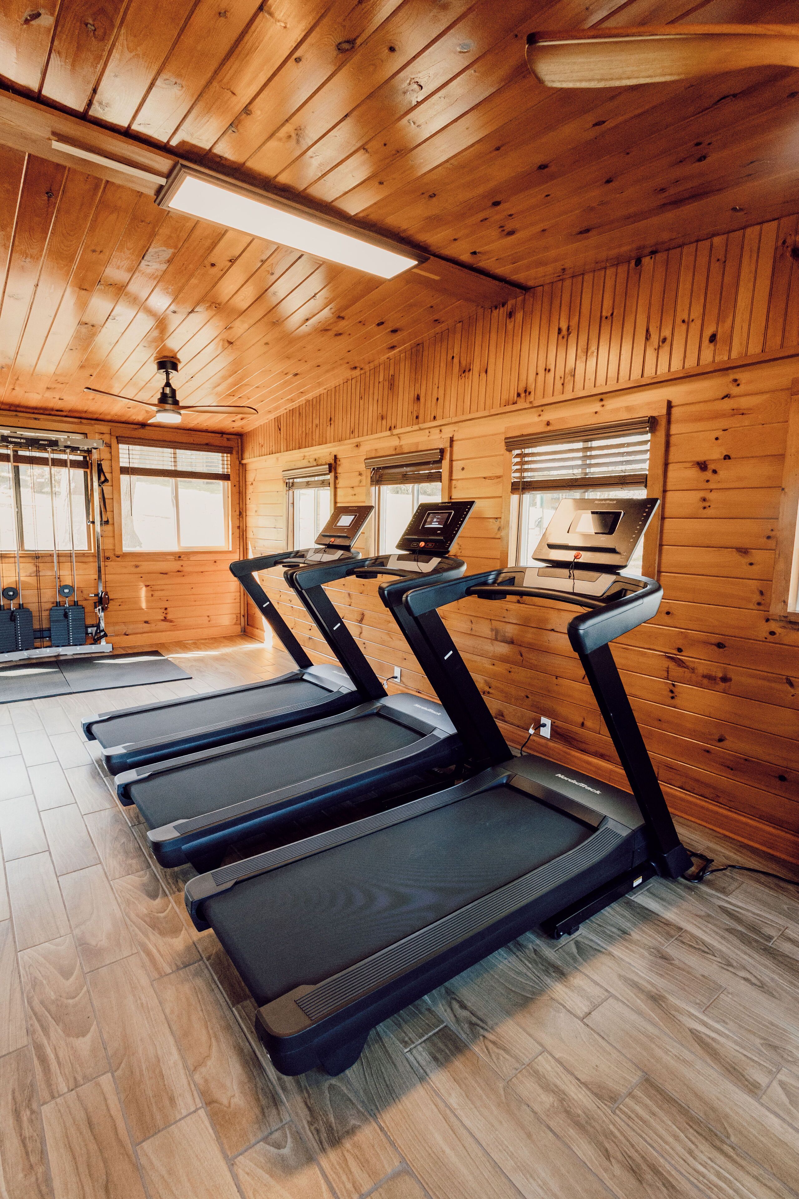 A gym with treadmills, exercise equipment, and wooden walls.