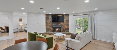 A modern living room with a stone fireplace, a dining area, and a seating area with a view of the outdoors.