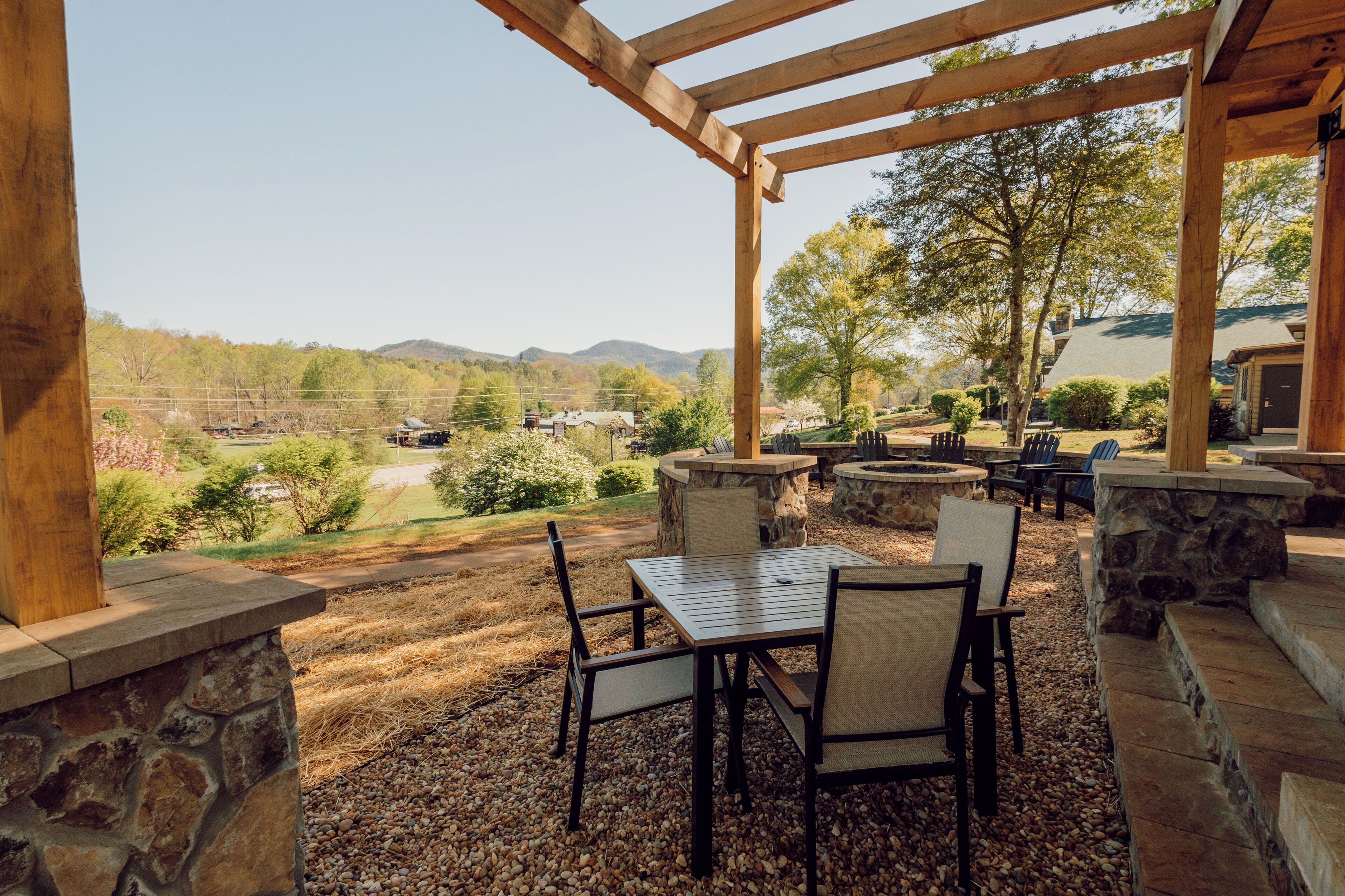 An outdoor patio with stone walls, a pergola, and a view of a mountainous landscape.