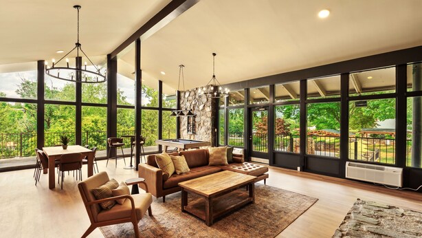 Amplia sala de estar con un sofá modular grande, una mesa de centro y una mesa de comedor. Amplias ventanas ofrecen vistas al exterior.