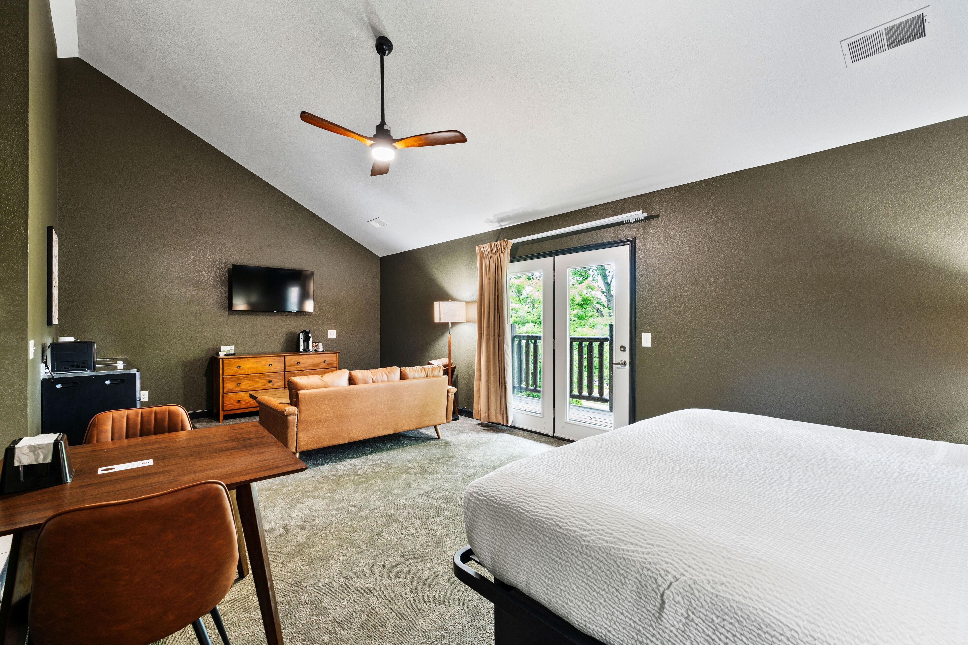 Habitación de hotel con cama, escritorio con silla, sofá, televisión y ventilador de techo.