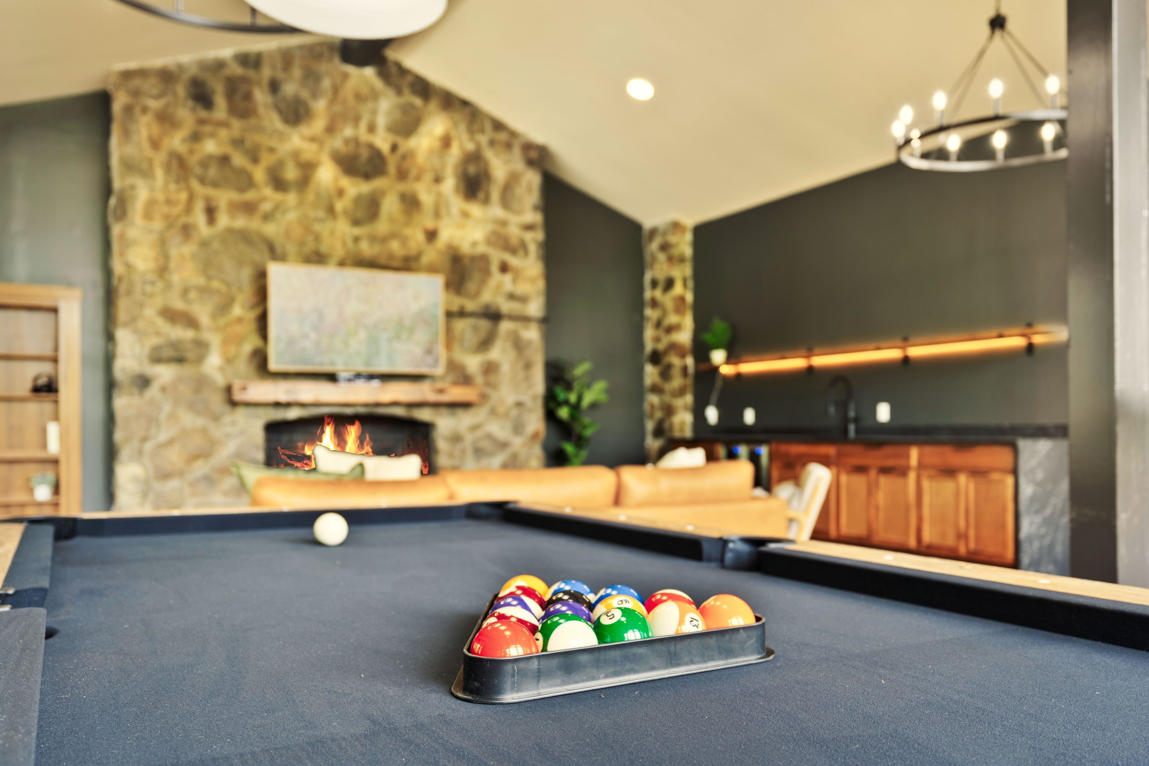 A pool table with billiard balls in a room with a stone wall, a fireplace, and a television mounted above it.
