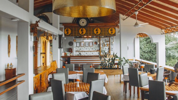 Un restaurant avec des tables et des chaises en bois, un coin bar et un grand luminaire suspendu.