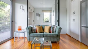 A modern living room with a green sofa, a glass coffee table, and a view through an open door to a balcony. - Athena's South Apartment (Alimos)