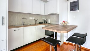 A modern kitchen with white cabinets, a wooden countertop, a coffee machine, and a bowl of fruit. There are two black bar stools at the counter. - Athena's South Apartment (Alimos)