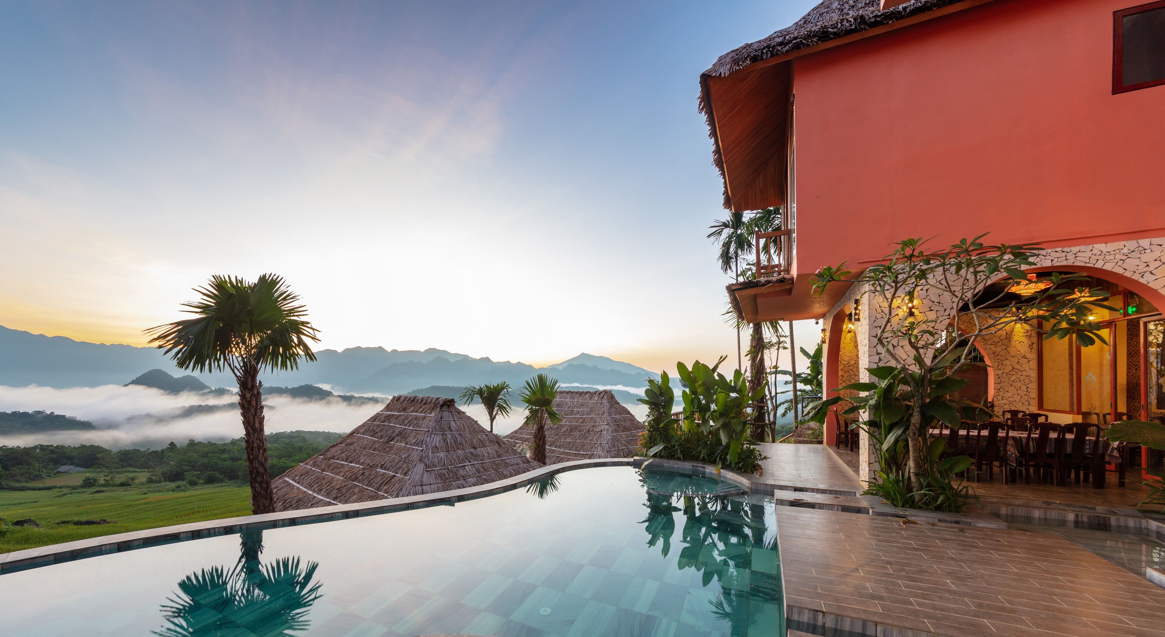 A resort with an infinity pool, a red building, and a view of mountains and clouds.