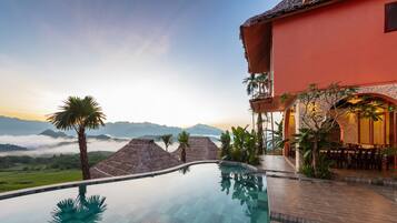 A resort with an infinity pool, a red building, and a view of mountains and clouds.