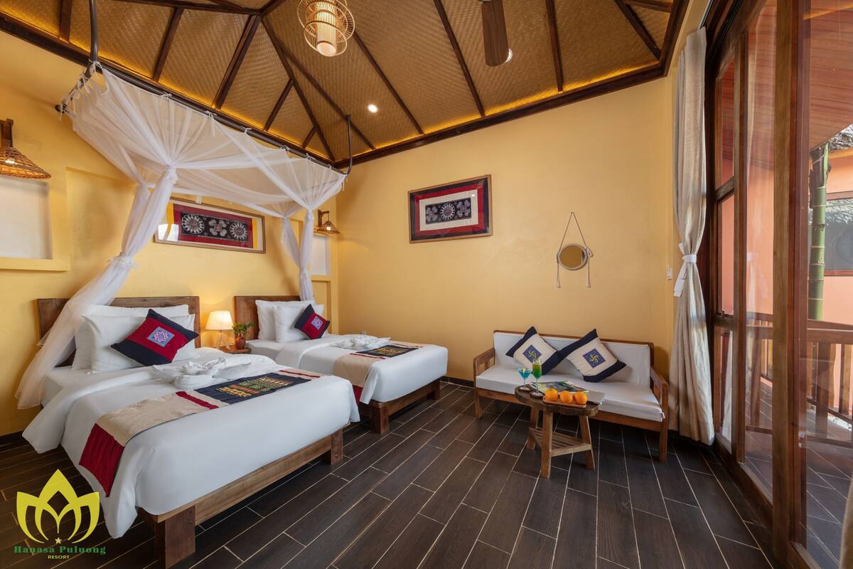 A hotel room with two beds, a sofa, a table with fruit, and a balcony with a view.