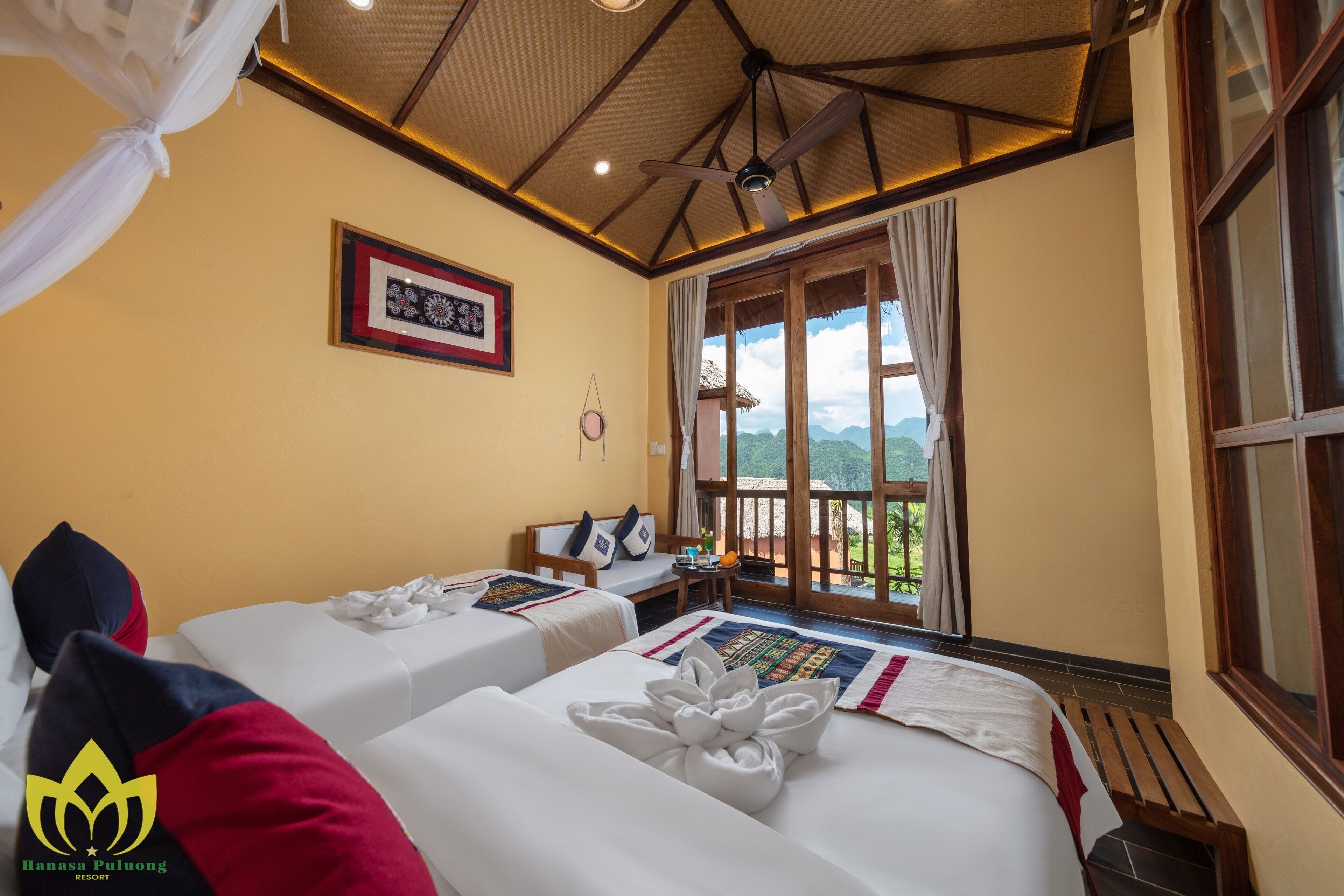 Habitación de hotel con dos camas, ventilador de techo, un cuadro enmarcado en la pared y una ventana con cortinas.