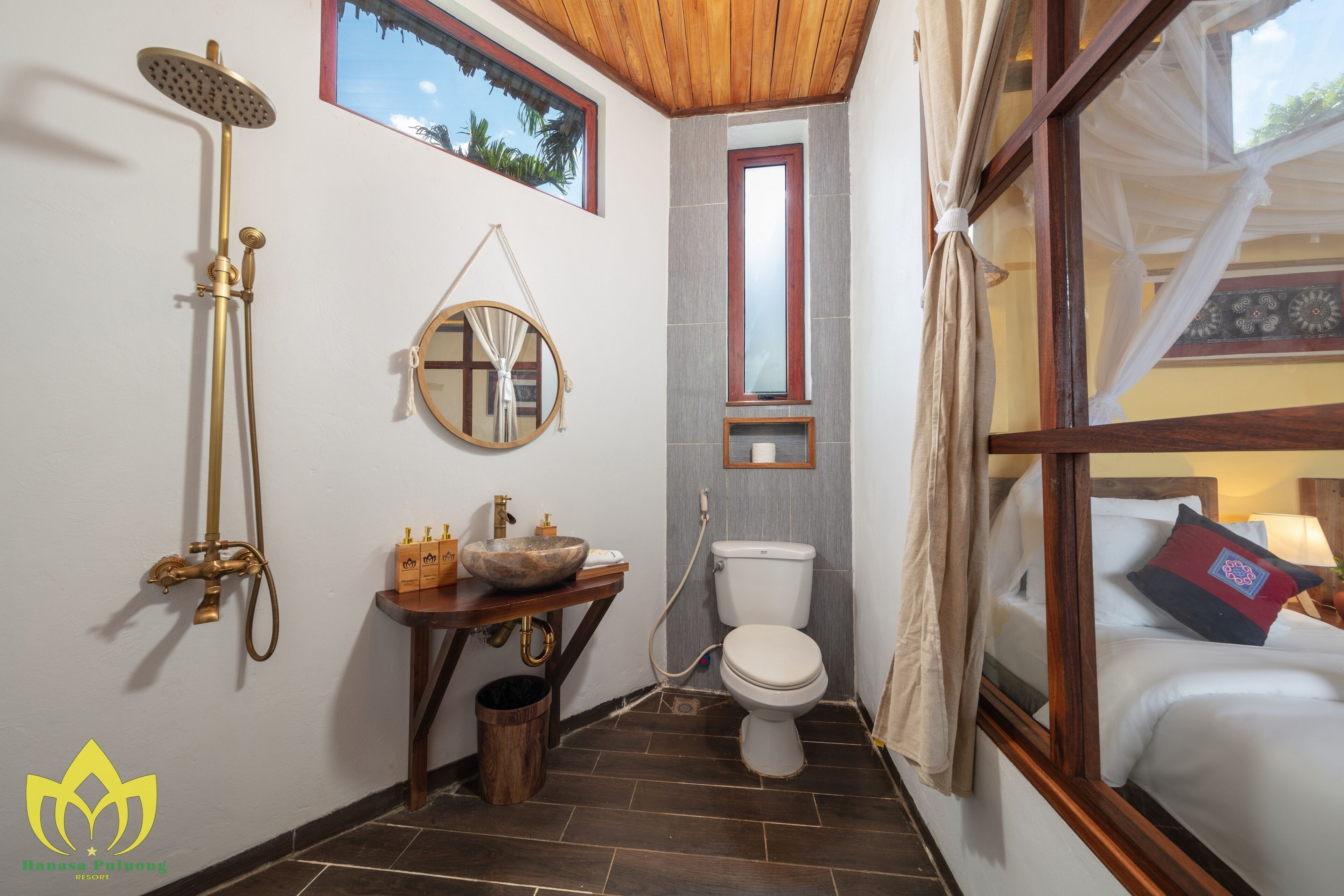 A bathroom with a wooden floor, a round mirror, a toilet, and a shower.