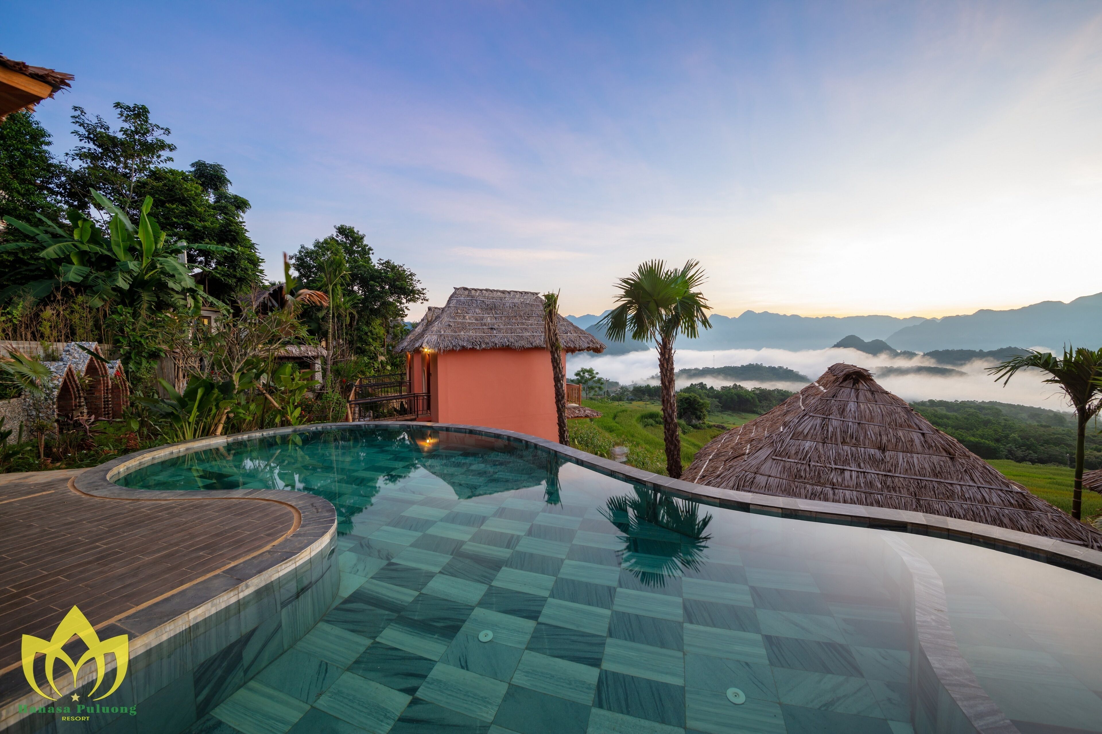 Une piscine d’un complexe hôtelier offrant une vue dégagée sur le paysage environnant, notamment une chaîne de montagnes et un bâtiment à toit de chaume.