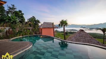 Une piscine d’un complexe hôtelier offrant une vue dégagée sur le paysage environnant, notamment une chaîne de montagnes et un bâtiment à toit de chaume.
