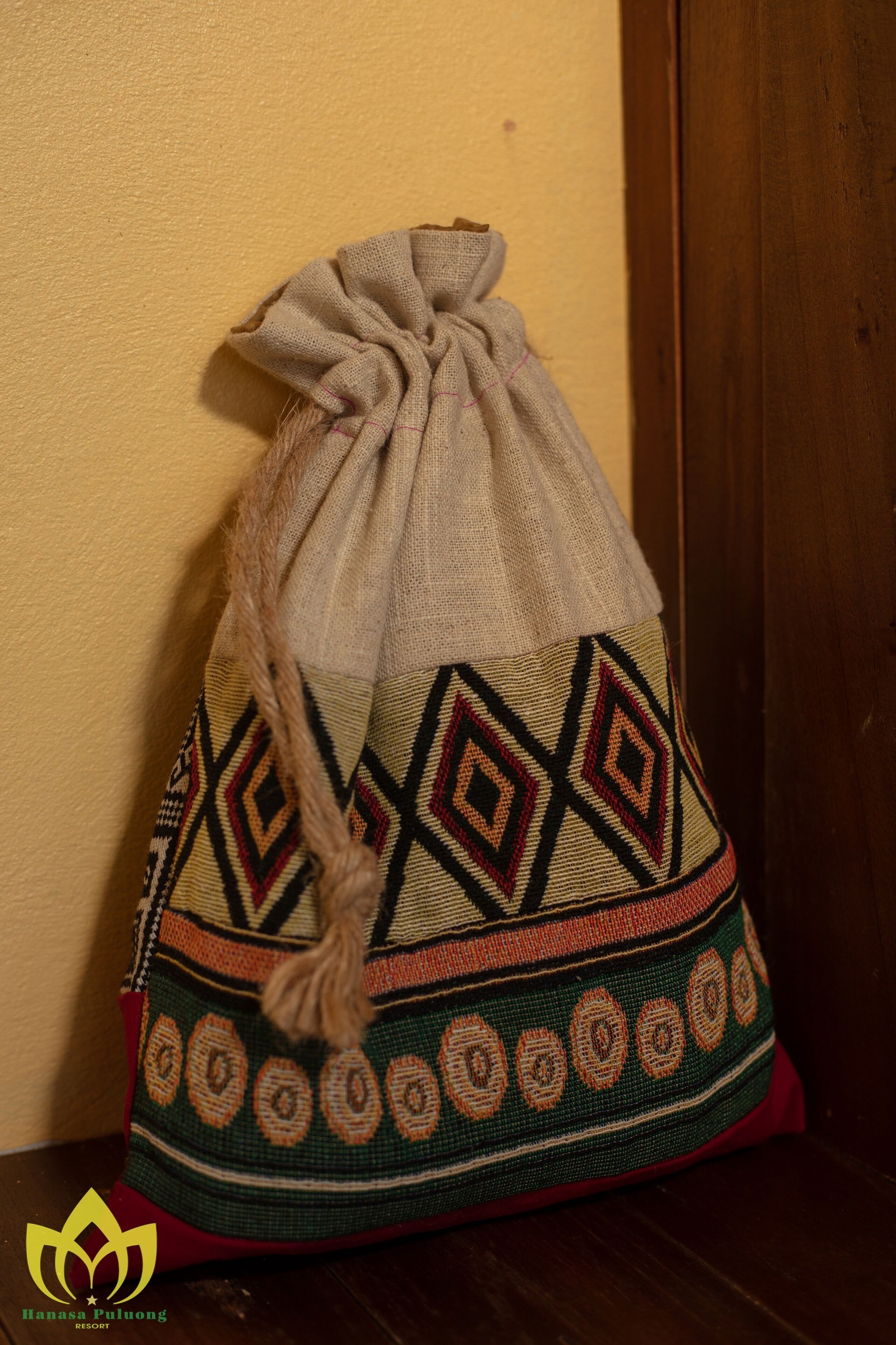 A drawstring bag with a geometric pattern and a tassel, placed against a yellow wall.