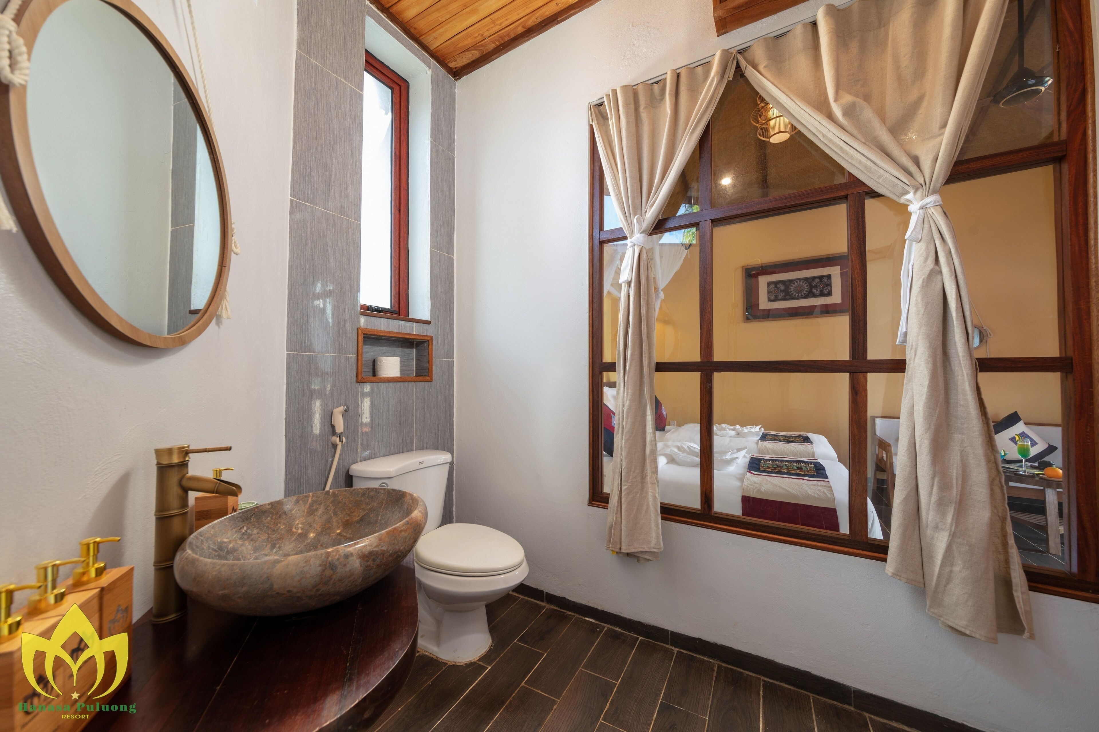 Ein Badezimmer mit einem großen, ovalen Waschbecken, einer Toilette, einem Spiegel und einem Fenster mit Vorhängen.