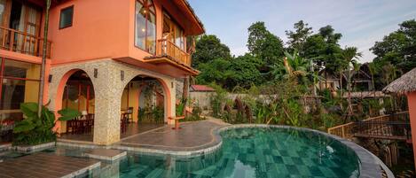 Ein Resort mit Swimmingpool, Sitzgelegenheiten im Freien und einem Gebäude mit Reetdach.