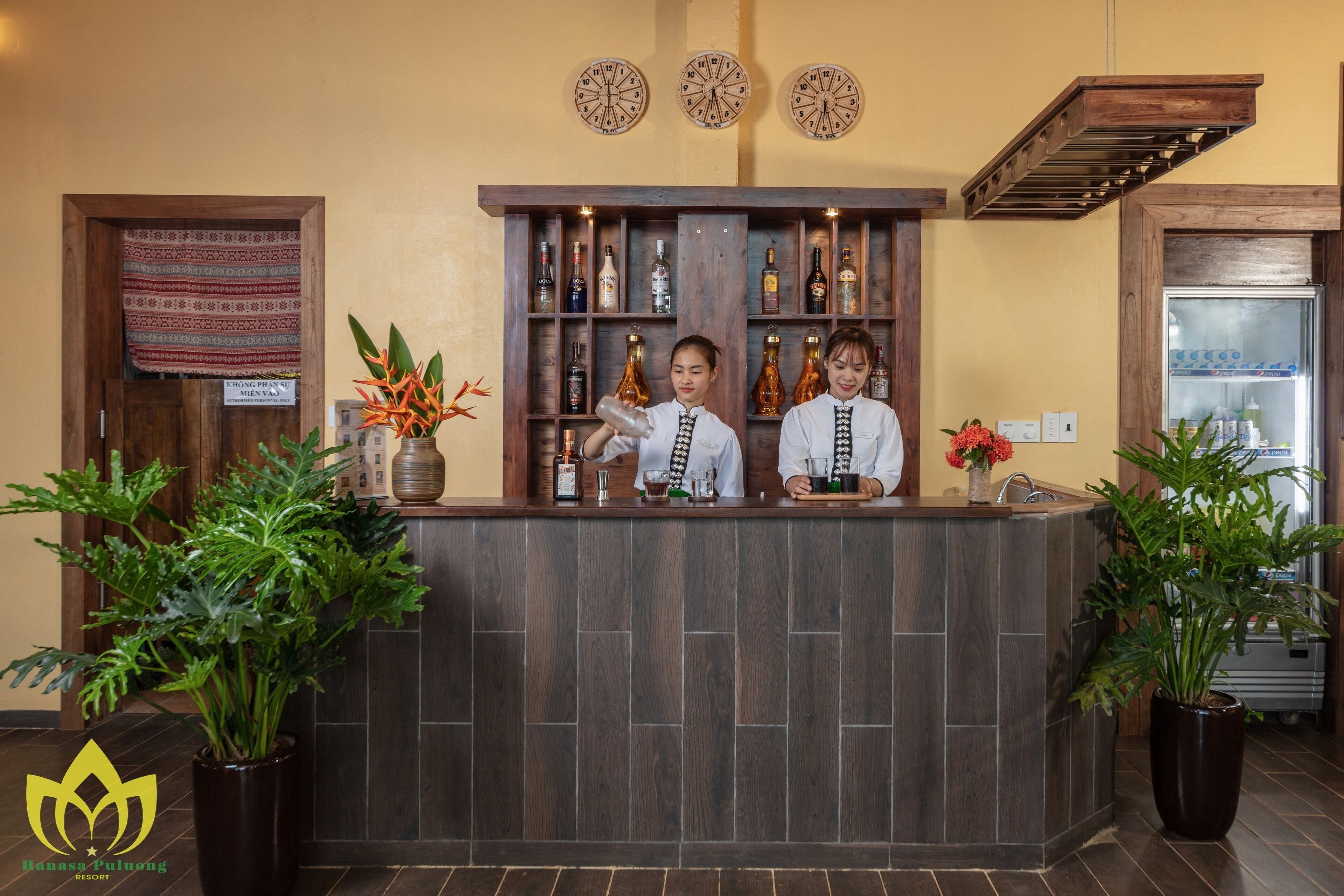A reception area with a wooden counter, two baristas, and a variety of bottles and glasses.