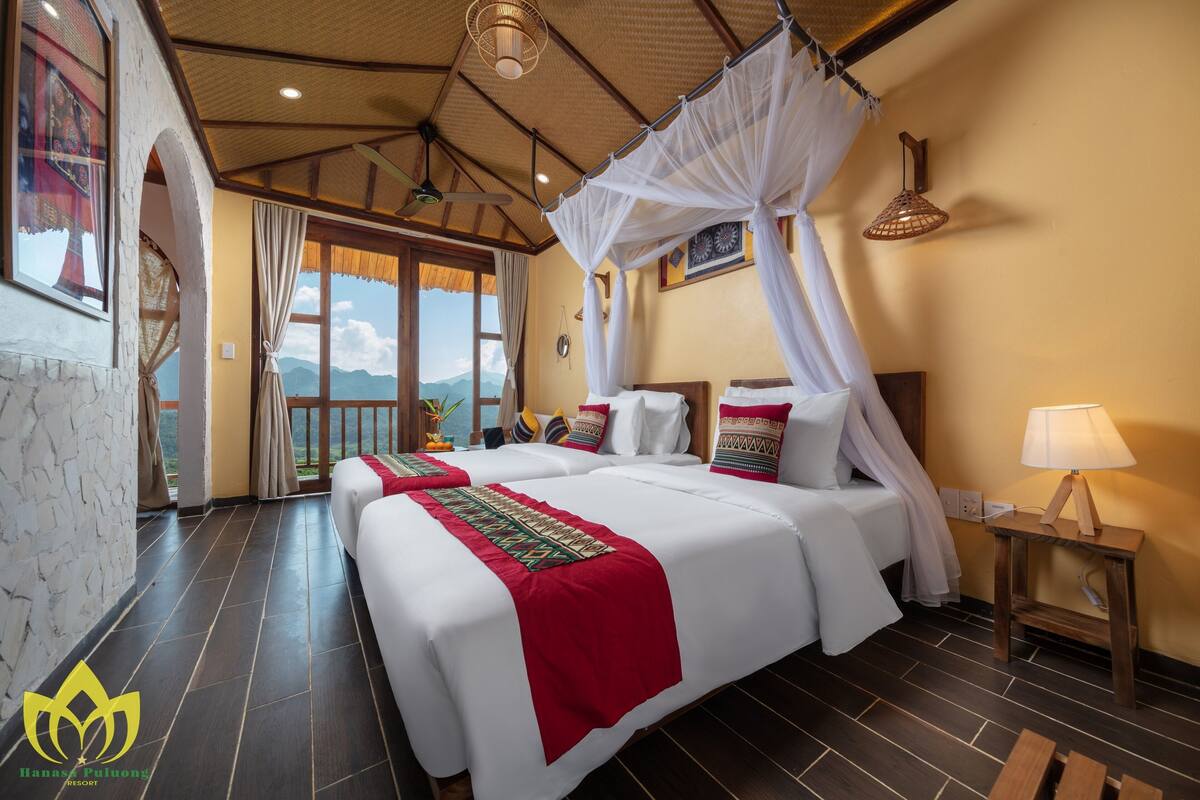 A hotel room with a large bed, a nightstand, a lamp, and a view of the mountains.