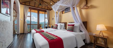 A hotel room with a large bed, a nightstand, a lamp, and a view of the mountains.