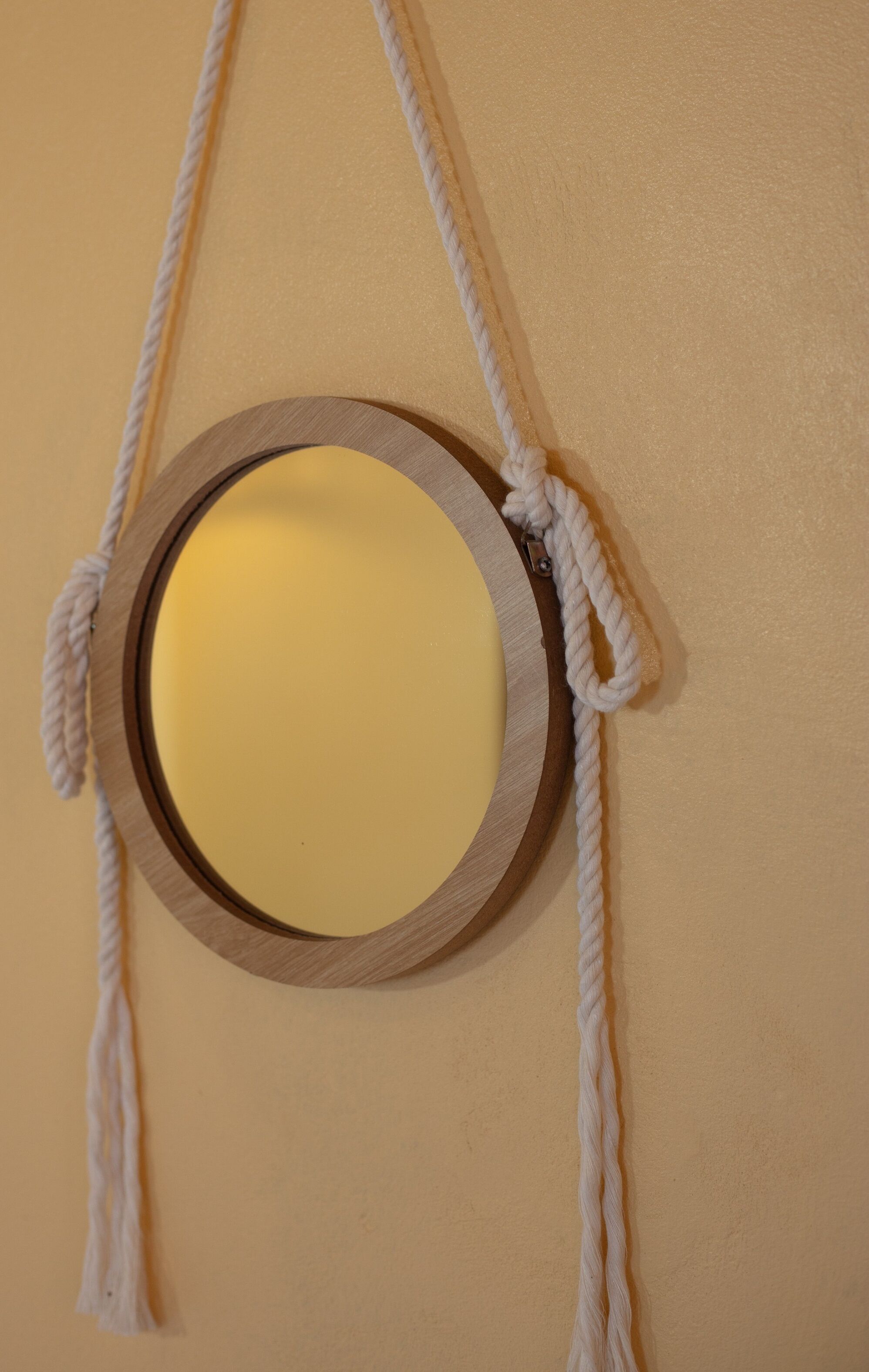 Un tapiz de macramé con un marco de madera circular y un objeto amarillo en su interior.