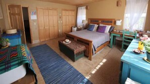 Ein gemütliches Schlafzimmer mit Holzbalkendecke, einem Bett mit Kopfteil, einem Nachttisch, einem Tisch mit Stuhl und einem Fenster mit Vorhängen.