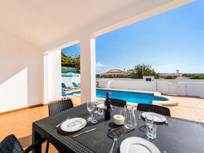 A dining table set for two with a pool view, outdoor chairs, and a clear sky.