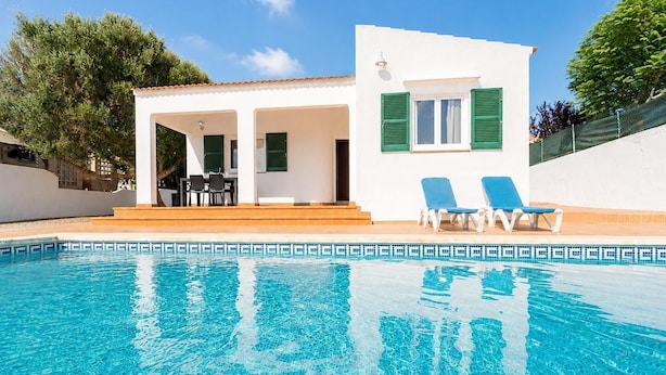 Une villa avec piscine, dotée d’une piscine à l’eau cristalline, d’une terrasse avec des chaises et d’un petit espace salon abrité.