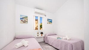 Une chambre avec deux lits, une fenêtre, un climatiseur et deux tableaux.