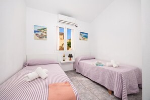 A room with two beds, a window, an air conditioner, and two paintings.