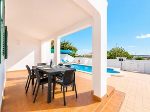 Um pátio externo com piscina, mesa e cadeiras, e vista para a paisagem ao redor.