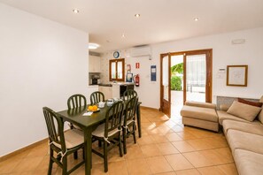 Ein Essbereich mit Tisch und Stühlen, eine Küchenzeile, eine Couch und eine Tür zum Balkon.