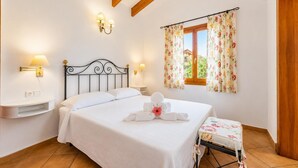 Ein Schlafzimmer mit einem Bett, Nachttischlampen, einem Fenster mit floralem Vorhang und einer Holzbalkendecke.