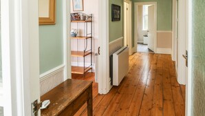 A hallway with wooden flooring, a radiator, and a shelf with books and a vase. - Tidal Reach (Paignton)