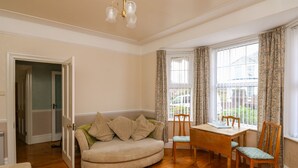 A cozy living room with a wooden floor, a sofa, a dining table with chairs, and a window with curtains. - Tidal Reach (Paignton)