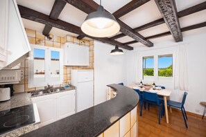 A modern kitchen with white cabinets, a black countertop, and a dining area with blue chairs. - Villa Eugenia Large Private Pool, A/C, WiFi (Cala en Porter)
