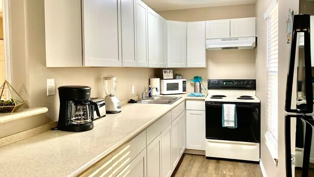 A compact kitchen with white cabinets, a black coffee maker, a microwave, a stove, and a refrigerator. - TRANQUILITY BAY-Spring /Summer /WINTER TEXAN FAVORITE!!  Come RELAX with us! (Aransas Pass)