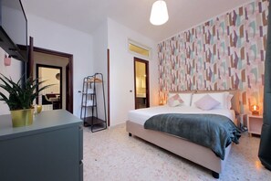 A modern bedroom with a bed, bedside tables, a dresser, a potted plant, and a patterned wall.