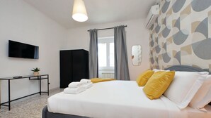 A modern hotel room with a bed, a flat-screen TV, a desk, and a window with curtains. - Comfy apartment next to Vatican city (Roma)