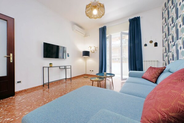A modern living room with a sofa, a small table, a TV mounted on the wall, and a patterned wall.