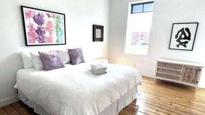Une chambre avec un grand lit, une commode et des œuvres d’art accrochées aux murs.