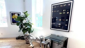 Une pièce avec un bureau en verre, une statue de zèbre, une grande plante et un tableau encadré représentant un bâtiment.