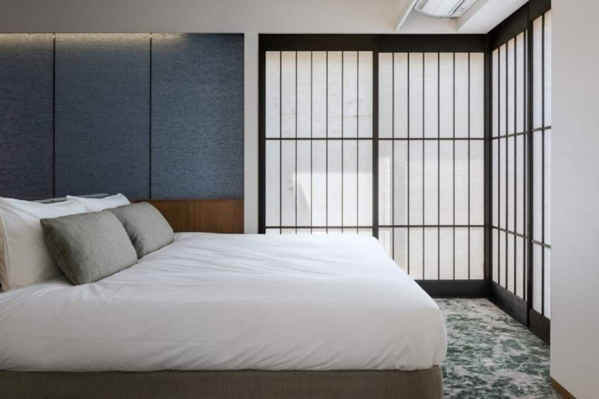 Quarto moderno com cama, travesseiros, mesa de cabeceira, abajur e uma janela grande com vista.